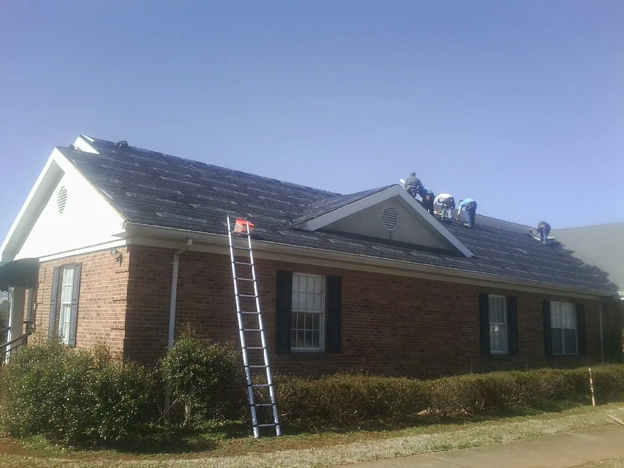 Crew tearing shingles off a brick ranch roof with a ladder set — Emergency Roof Repair work by our crew in Bingen