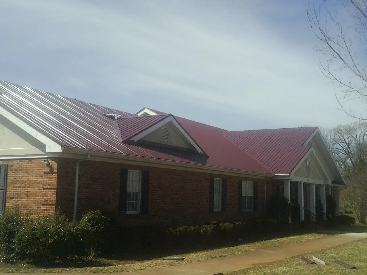 Red metal roof with gabled entries on a long brick building, from a Hail Damage Roof Repair job in Bingen