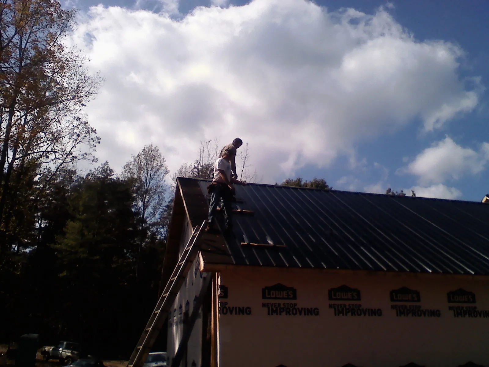 Roofer fastening dark metal panels high against a cloudy sky, from a Roof Inspection job in Bingen