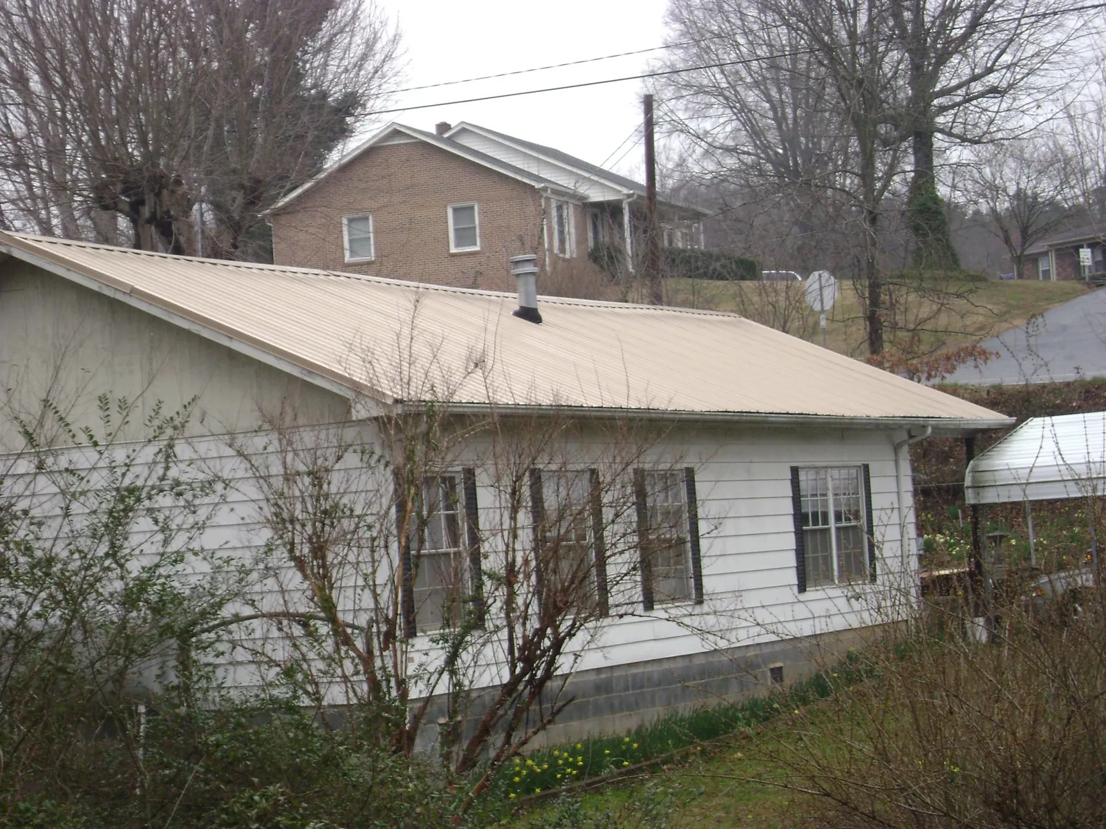 Tan metal roof on a white sided house set into a hillside — Commercial Roofing by Roofing Brothers in Bingen